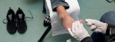Et menneske får hjælp til at pleje et sår på sin tå i et af Kirkens Korshærs sundhedsrum