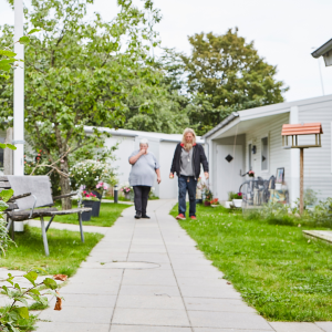 Mand og kvinde går ned ad en grøn sti i Kirkens Korshærs skæve boliger Skurbyen i Aalborg, hvor tidligere hjemløse får en værdig bolig