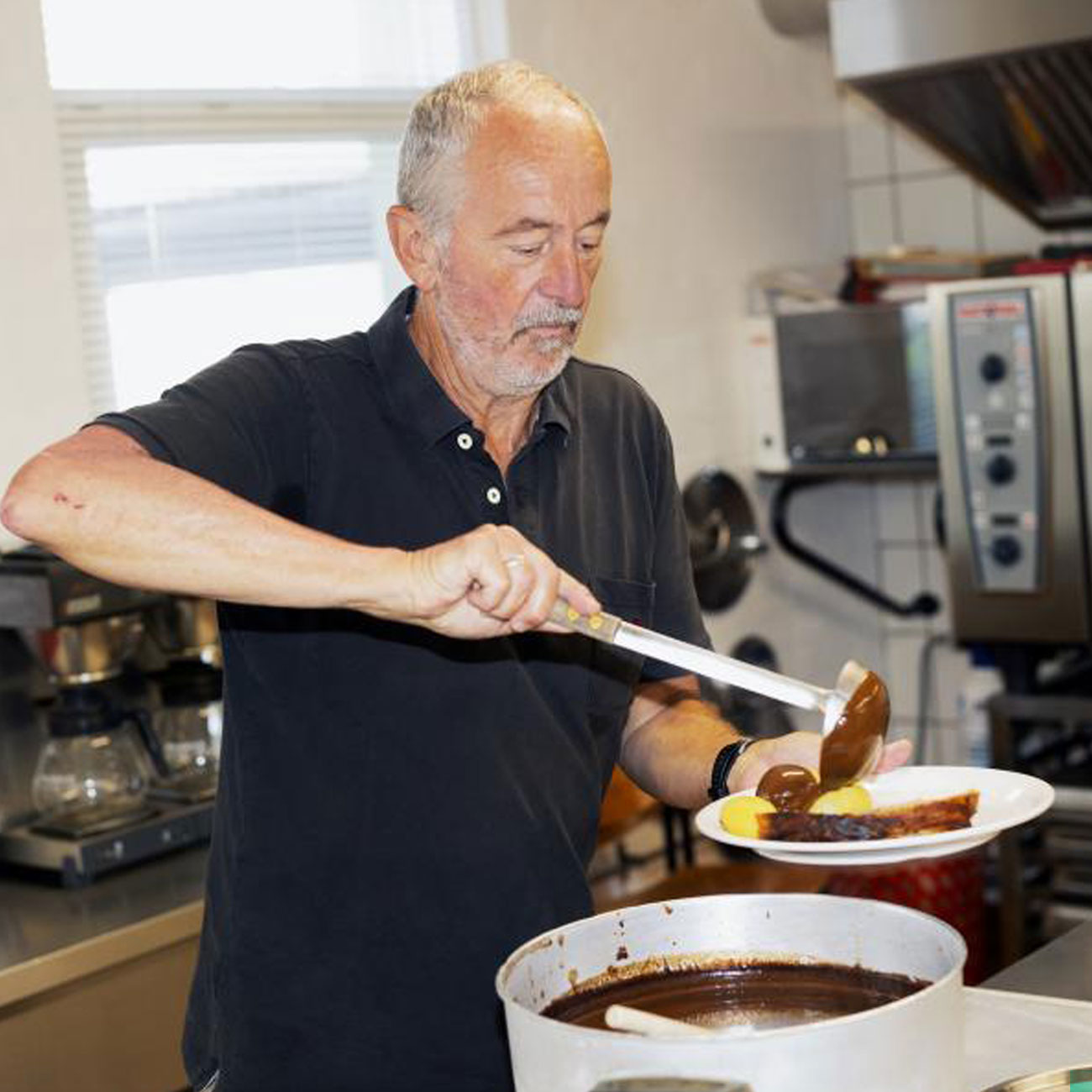 En frivillig serverer sovs og kartofler på en varmestue