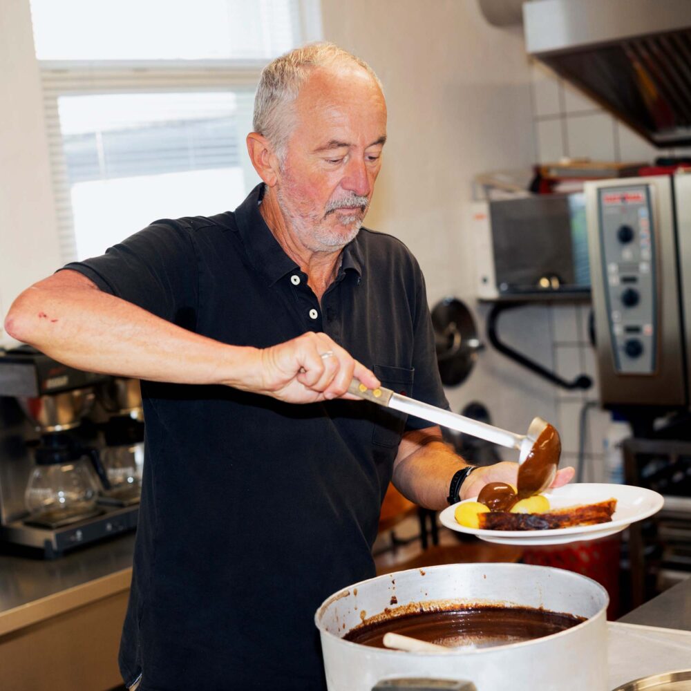 En frivillig i det sociale arbejde øser et varmt måltid op