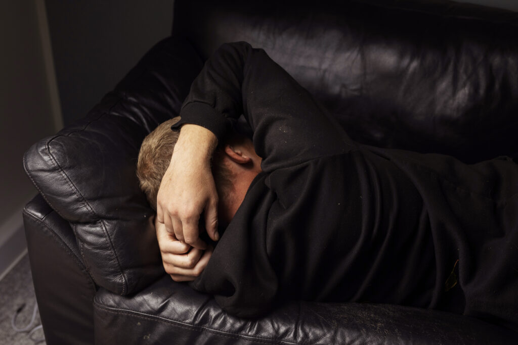 En person ligger sammenkrøbet på en mørk lædersofa med armen over hovedet i et dæmpet rum.