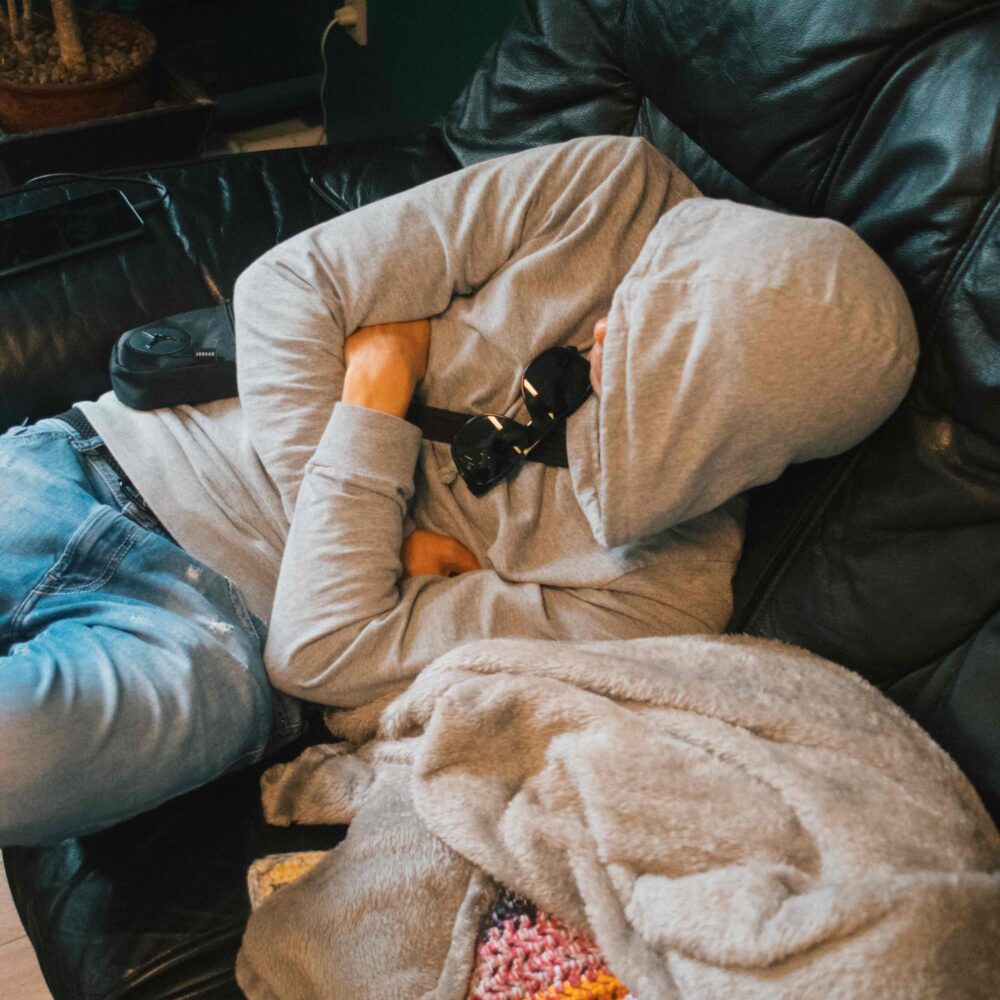 En mand sidder i en sofa og sover med en hætte over ansigtet