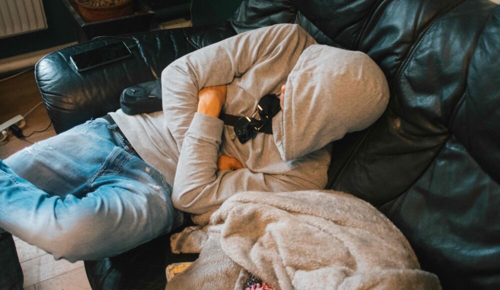 En mand sidder i en sofa og sover med en hætte over ansigtet